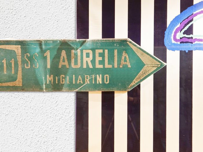 Immagine di Segnali dallo Spazio: un cartello verde Aurelia Migliarino e dettagli dipinti su fondo a righe